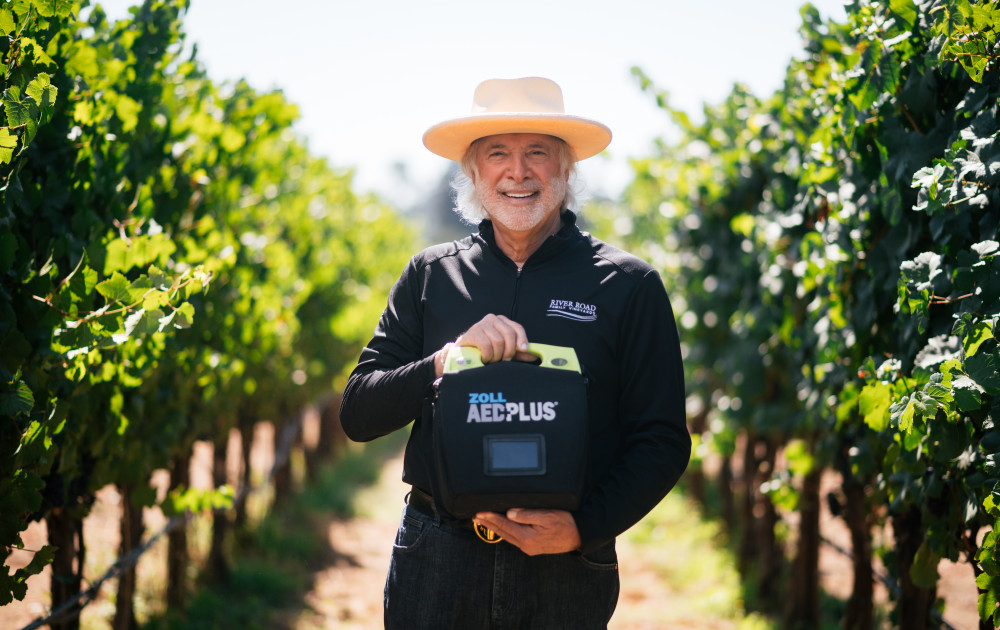 Ron Rubin standing in between vineyard rows holding an AED